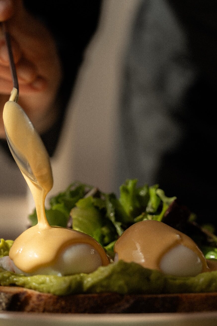 Hollandaise sauce being poured over poached eggs at Mykonos Brunch Club